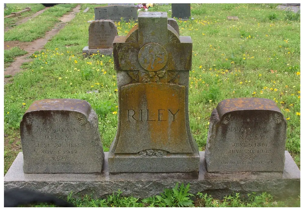 Grave marker for the Riley family in a cemetery, showing a central 'RILEY' headstone with a carved cross and floral motif flanked by two footstones inscribed 'FATHER JOHN JOSEPH RILEY JUNE 24 1835 NOV 1 1917' and 'MOTHER MARGARET ELLEN RILEY JUNE 6 1861 JUNE 20 1942'; other headstones including one reading 'LOUISE RILEY' are visible in the grassy background.
