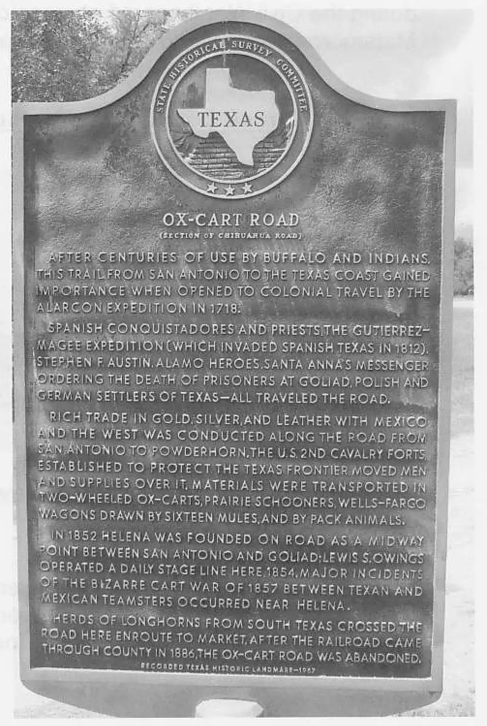 Photograph of the Texas Historical Marker titled 'OX-CART ROAD (Section of Chihuahua Road)', describing the history of the trade road through Helena.
