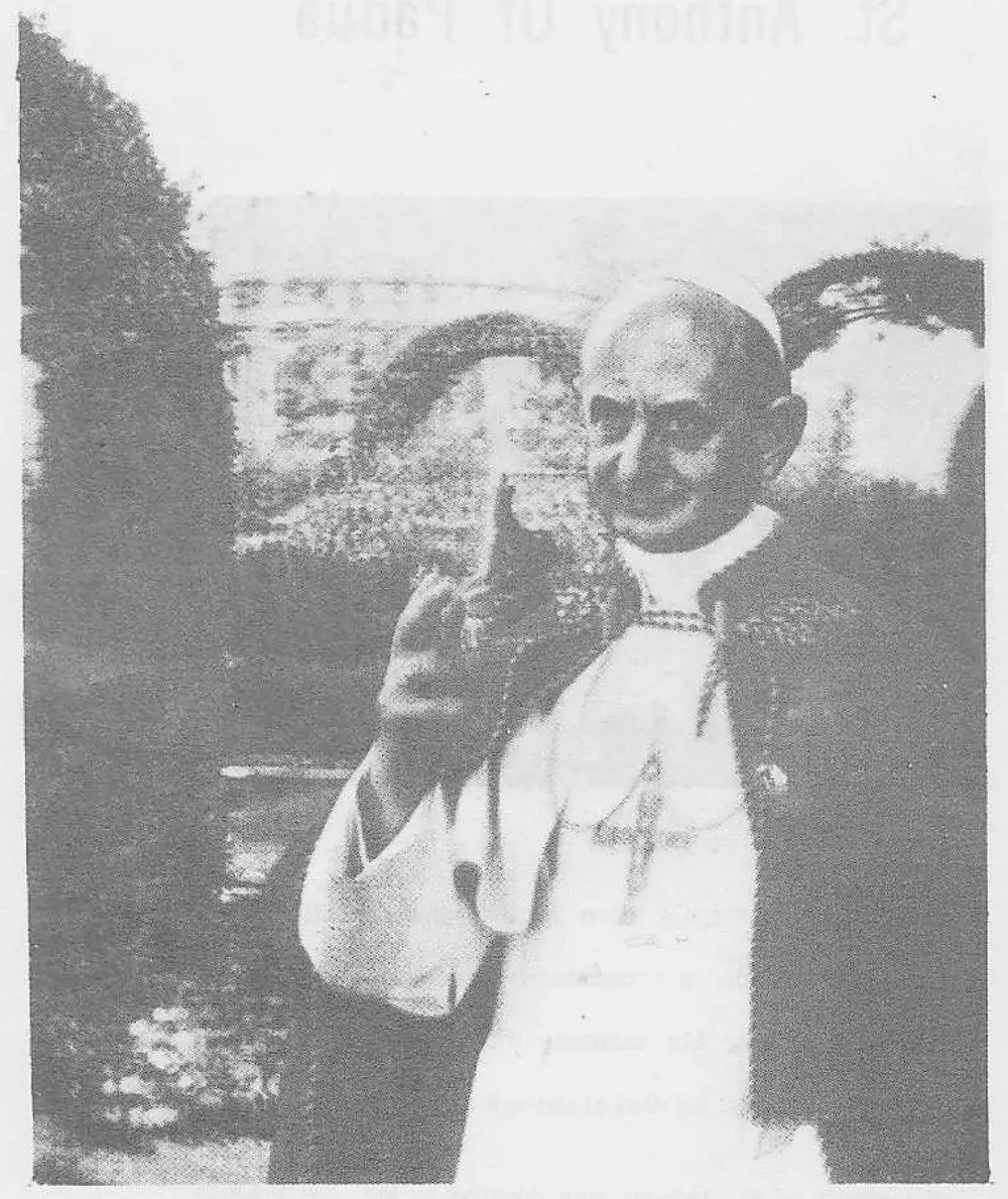 Photograph of Pope Paul, bald, wearing white papal cassock and pectoral cross, holding a rosary, standing outdoors in a garden setting.