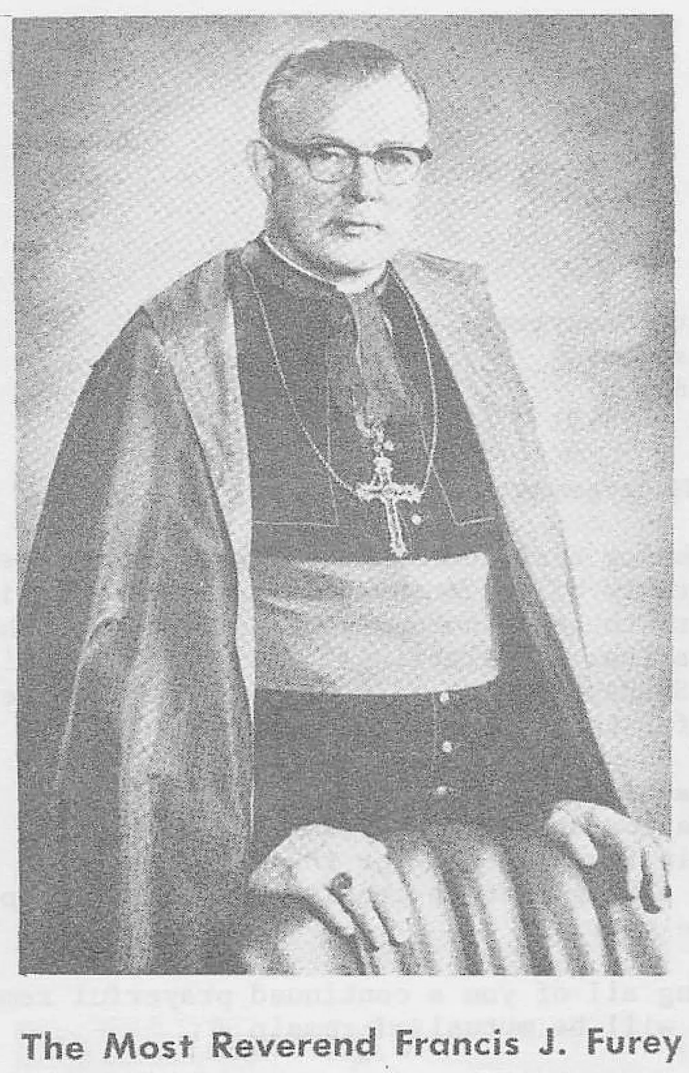 Formal portrait photograph of a bishop wearing glasses, a cape, zucchetto-less cassock with sash, and a pectoral cross, seated with hand resting on an armrest.