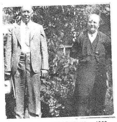 A standing man and woman posed outdoors amid bushes