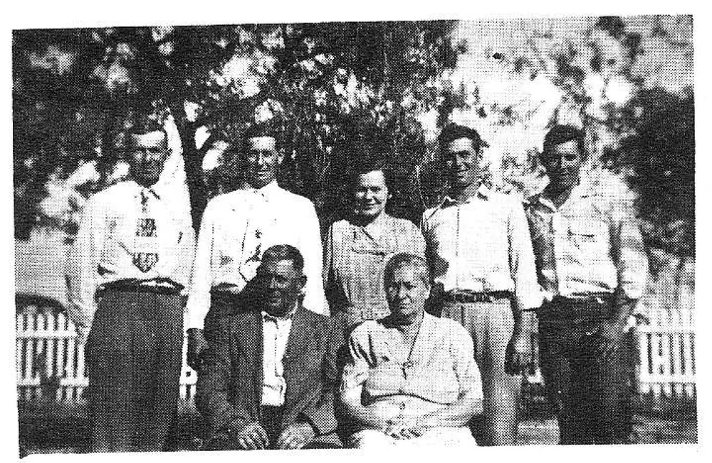 Group photo of the Will Yanta family posing outdoors in front of a tree and picket fence; five men standing, two seated (one man, one woman).