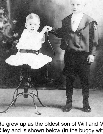 A toddler seated on a stand and an older boy standing beside, both formally dressed for a studio portrait.