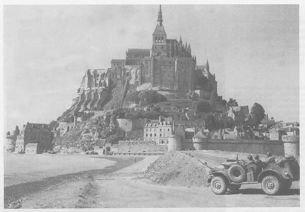 Aerial/distant view of Mont Saint-Michel with a US military vehicle (armored car with mounted gun) in the foreground on a road, taken during WWII.