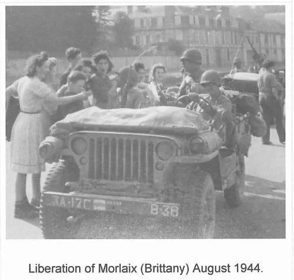 A jeep with license plate 3A-17C, B-38 surrounded by cheering civilians, mostly women, greeting soldiers during the liberation of Morlaix.