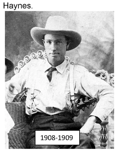 Photograph of a man wearing a wide-brimmed hat, suspenders, and tie, seated in a wicker chair.